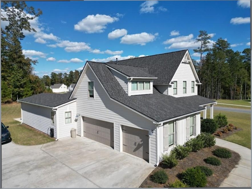 A white home with dark shingle roofing, a driveway, and landscaped grounds.